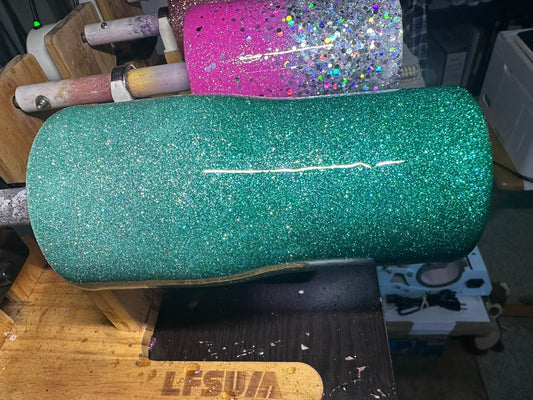 A green glitter tumbler spinning on a tumbler turner, freshly coated with epoxy, as it cures for a smooth, glossy finish.