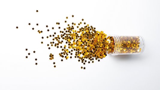 Gold star-shaped glitter spilling from a container, creating a sparkling and dreamy aesthetic.