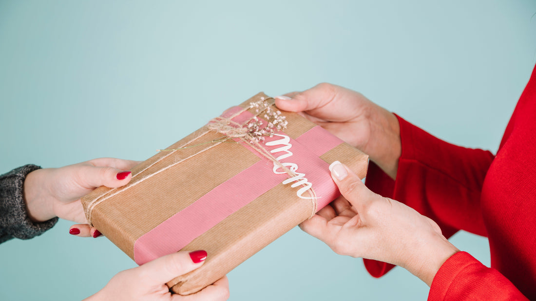 Hands exchanging a beautifully wrapped gift with 'Mom' written on the tag, symbolizing a heartfelt and personalized present.