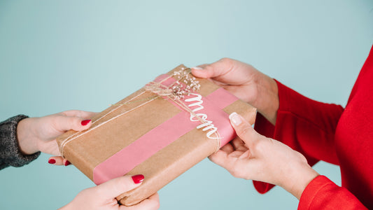 Hands exchanging a beautifully wrapped gift with 'Mom' written on the tag, symbolizing a heartfelt and personalized present.